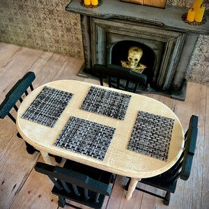 May include: A white oval table with four black chairs. The table has four black and white woven placemats. The table is set in a room with a fireplace and a spooky Halloween theme.