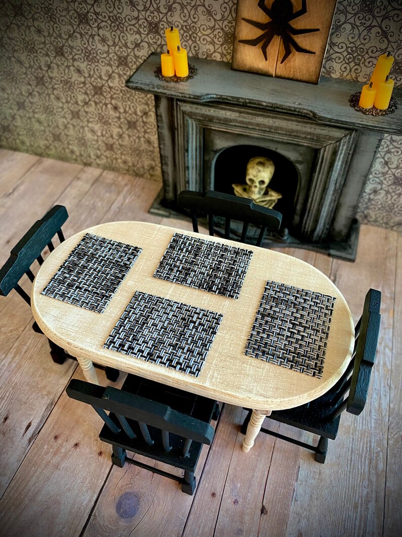 May include: A white oval table with four black chairs. The table has four black and white woven placemats. The table is set in a room with a fireplace and a spooky Halloween theme.