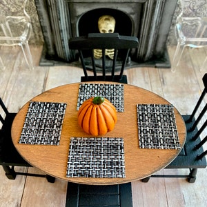 May include: A wooden table with black chairs and a pumpkin centerpiece. The table is set with black and white placemats.