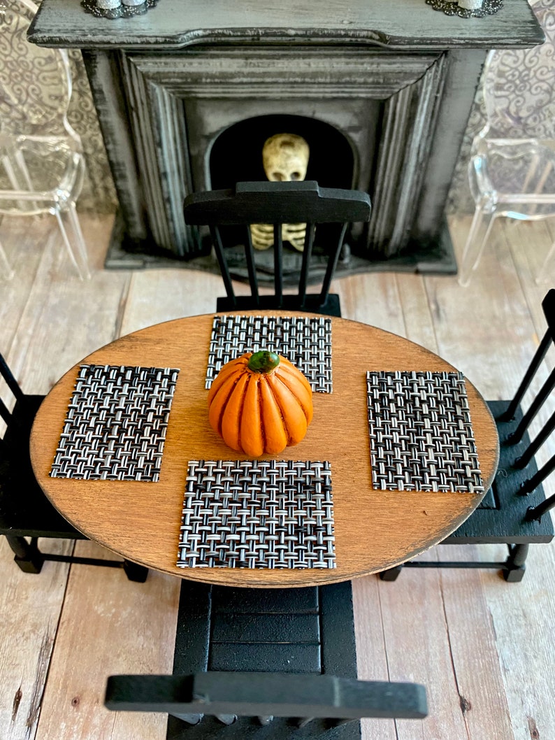 May include: A wooden table with black chairs and a pumpkin centerpiece. The table is set with black and white placemats.