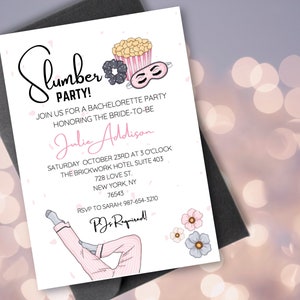 May include: A white invitation card with pink and black illustrations. The text on the card reads "Slumber Party!" and includes details for a bachelorette party for Julie Addison. The party is scheduled for Saturday, October 23rd at 3 o'clock at The Brickwork Hotel, Suite 403, 728 Love St., New York, NY 76543. The RSVP information is provided with a phone number and the text "PJs Required!"