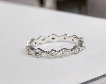May include: A silver band ring with a row of small diamonds set in a geometric pattern.