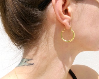 May include: Gold hoop earrings worn in a person's ear. The earrings are simple and classic.