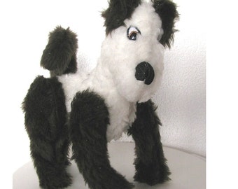 May include: A black and white plush dog toy with brown fur. The dog is sitting with its legs crossed and its head tilted to the side. The dog has a black nose and black eyes.