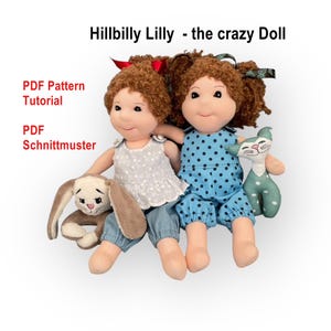 May include: Two handmade rag dolls with curly brown hair, wearing different outfits. One doll is in a blue polka-dot jumpsuit, the other in a white top and blue pants. A stuffed bunny and a cat are also present. Text reads "Hillbilly Lilly - the crazy Doll".