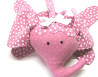 May include: A pink fabric elephant with white polka dots, hanging from a loop. The elephant has a white bow on its head and black eyes.