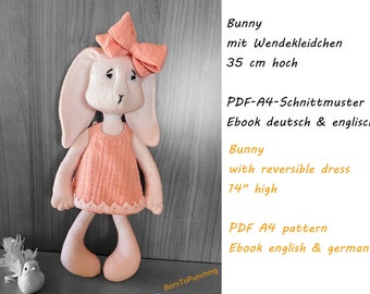May include: A pink bunny doll with a reversible dress, 14 inches tall. The doll is wearing a pink dress with a white lace trim. The doll is standing on a wooden surface. The text "Bunny with reversible dress 14" high PDF A4 pattern Ebook english & german" is visible in the image.