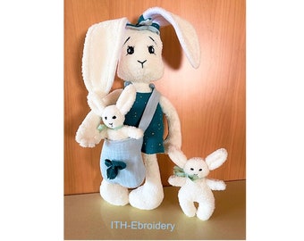 May include: Three white plush bunny toys. The largest bunny is wearing a teal and gold dress and carrying a smaller bunny in a light blue bag. The smallest bunny is standing on its own.