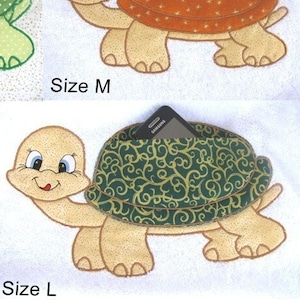 Può includere: Disegni di tartarughe applicati nelle taglie S, M e L. Le tartarughe hanno facce sorridenti e gusci a fantasia in verde, arancione e verde con volute dorate. Sono mostrati anche una tasca a forma di tartaruga verde e due asciugamani bianchi con disegni di tartarughe.