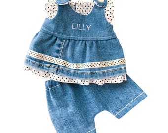 May include: A denim doll outfit, including a top and shorts. The top features a ruffled white polka dot trim and the name "LILLY" embroidered on the front. The outfit is designed for a 15-inch doll.