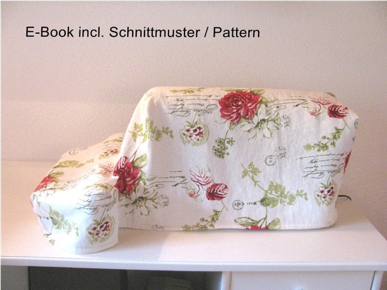 May include: A white sewing machine cover with a floral pattern featuring red roses and green leaves. The cover has a white background with a subtle script pattern. The text "E-Book incl. Schnittmuster / Pattern" is visible at the top of the image.