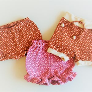 May include: Three pairs of toddler shorts in a polka dot pattern. One pair is rust orange with white dots, one pair is pink with white dots, and one pair is rust orange with white dots and a white waistband.