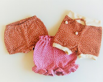 May include: Three pairs of toddler shorts in a polka dot pattern. One pair is rust orange with white dots, one pair is pink with white dots, and one pair is rust orange with white dots and a white waistband.