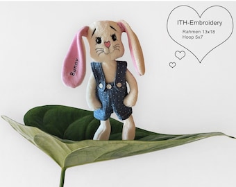 May include: A white plush bunny wearing blue overalls with white polka dots. The bunny has pink ears with the word "Bunny" embroidered on one ear. The bunny is sitting on a green leaf. The image includes the text "ITH-Embroidery Rahmen 13x18 Hoop 5x7".