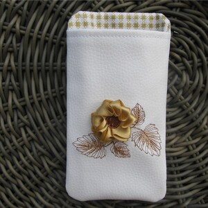 May include: White leather phone case with a gold embroidered flower and leaves.