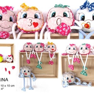 May include: Five colorful plush toys with embroidered faces and legs. The toys are hanging from a wooden shelf. The toys are 4 inches in diameter and the shelf is 10 inches by 10 inches. The text "PALLINA" is written on the shelf. The text "Rahmen 10 x 10 cm" and "Hoop 4 x 4" is also written on the shelf.