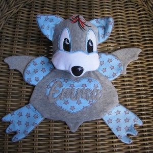 May include: A gray and blue plush bat with a white face and embroidered blue stars. The bat has a heart-shaped patch with the name "Emma" embroidered on it.