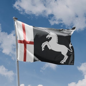 Könnte beinhalten: Eine weiße Flagge mit einem roten Kreuz auf der linken Seite und einem schwarzen Einhorn auf der rechten Seite. Die Flagge weht im Wind vor einem blauen Himmel mit weißen Wolken.