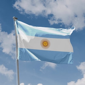 Op de afbeelding: Een blauwe en witte vlag met een gele zon in het midden, wapperen in de wind tegen een blauwe lucht met witte wolken.