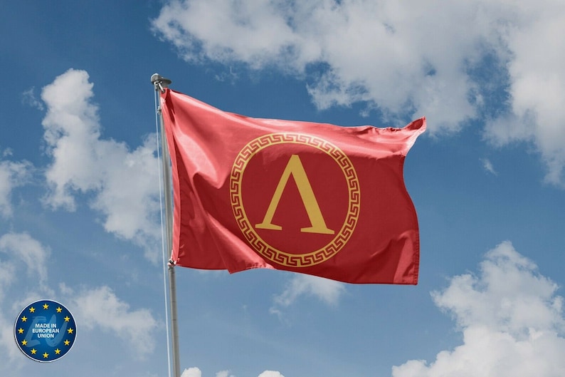 May include: A red flag with a gold Greek letter lambda in a circle with a gold meander pattern. The flag is waving in the wind against a blue sky with white clouds.