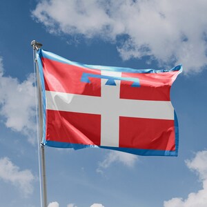 Puede incluir: Bandera del Valle de Aosta, Italia, con una cruz blanca sobre fondo rojo, borde y emblema azules. La bandera ondea contra un cielo azul con nubes. Un emblema "Made in European Union" es visible en la esquina inferior izquierda.