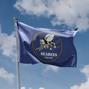 May include: A blue flag with a yellow rope border and a yellow circle in the center. The circle contains a cartoon bee wearing a sailor hat and holding a gun. The text "Seabees" and "Can Do!" is printed below the bee.