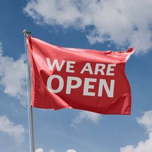 May include: A red flag with the words "We Are Open" in white letters against a blue sky with white clouds.