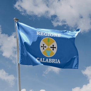 Könnte beinhalten: Eine blaue Flagge der Region Kalabrien in Italien, die im Wind vor einem teilweise bewölkten Himmel weht. Die Flagge trägt die Worte "REGIONE CALABRIA" und ein zentrales Emblem mit einem Baum, Kreuzen und einem gelben Kreis.