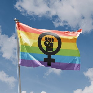 May include: A rainbow flag featuring a black fist within a female symbol, fluttering in the breeze against a blue sky with clouds. The flag symbolises LGBTQ+ and feminist solidarity. A small emblem on the bottom left reads "Made in European Union."