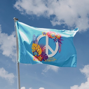 Op de afbeelding: Een blauwe vlag met een wit vredesteken omringd door kleurrijke bloemen en bladeren. De vlag wappert in de wind tegen een blauwe lucht met witte wolken.