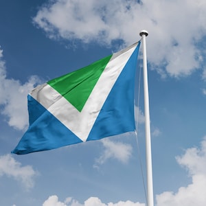 May include: A blue, white, and green flag with a white chevron shape and a green triangle inside the chevron. The flag is flying on a white flagpole against a blue sky with white clouds.