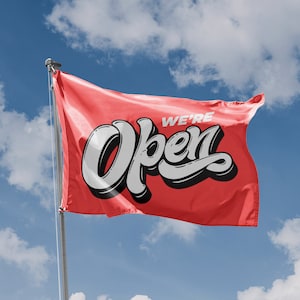 May include: A red flag with the words "We're Open" in white and black lettering against a blue sky.