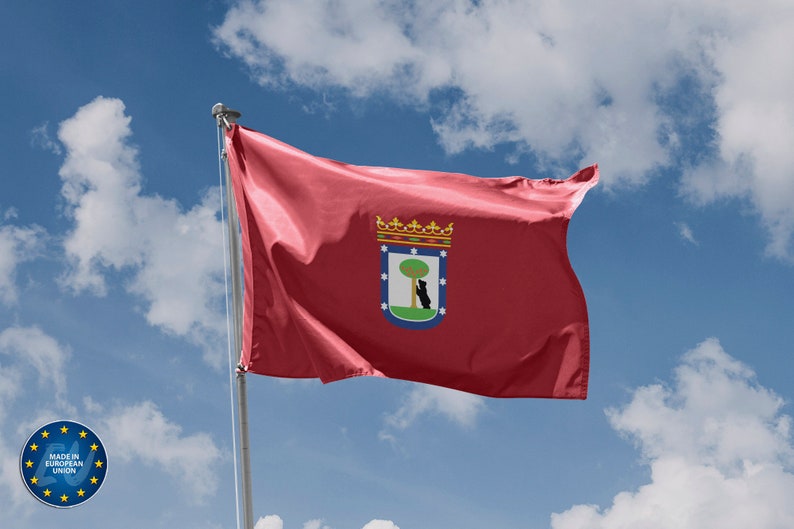 May include: A red flag with a coat of arms featuring a green tree and a black bear, against a blue sky with white clouds.