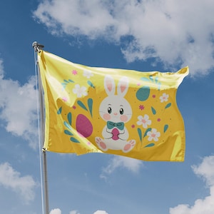 May include: A yellow flag featuring a white bunny holding a pink Easter egg. The bunny is wearing a blue bow tie. The flag is decorated with green leaves, white flowers, and yellow Easter eggs.