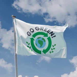 Può includere: Una bandiera bianca con un simbolo di riciclaggio verde e le parole "GO GREEN!" stampate su di essa. Il simbolo presenta un globo terrestre blu con frecce verdi che lo circondano. La bandiera sventola al vento contro un cielo blu con nuvole bianche.