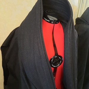 May include: A black hooded robe with a red mannequin inside. The mannequin has a black measuring tape around its neck with the word "SOSTYLISTH" printed on it.