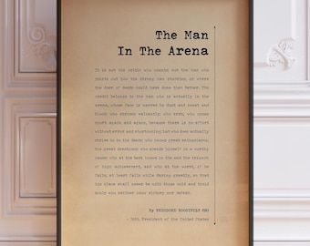 Op de afbeelding: Een ingelijste print op beige papier met de tekst The Man In The Arena van Theodore Roosevelt. Het zwarte lettertype in typemachinestijl bevat de titel, de volledige toespraak en de toeschrijving aan de 26e president van de VS.