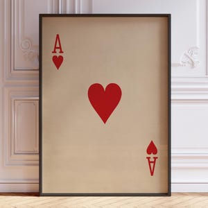May include: A framed wall art print featuring the Ace of Hearts playing card design. The print has a beige background with a large red heart in the center, and the letter A with a small red heart symbol in the top left and bottom right corners.