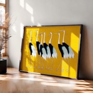 Op de afbeelding: Een ingelijst rechthoekig wandkunstwerk met een levendige mosterdgele achtergrond en een herhalende illustratie van zes witte en zwarte kraanvogels die op een rij staan, elk met lange dunne poten en een rode vlek op de kop.