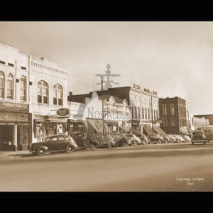 May include: Sepia-toned photograph of a street scene in LaGrange, Georgia, from 1943. Classic cars are parked along the curb in front of storefronts. The sign for "Nostalgia Station" is visible.