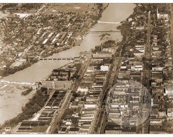 May include: An aerial view of Columbus, Georgia in 1913. The photo shows a river with two bridges, a large industrial complex, and a dense urban area.