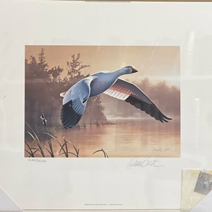May include: A framed print of a white goose in flight over a lake at sunset. The print is signed by the artist, David S.  Smith, and numbered 16/200.