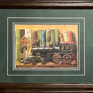 May include: Framed artwork featuring a detailed illustration of a vintage steam train in front of a bookshelf. The train is black with red accents, and a railroad crossing sign is visible. The background includes a variety of colorful books.