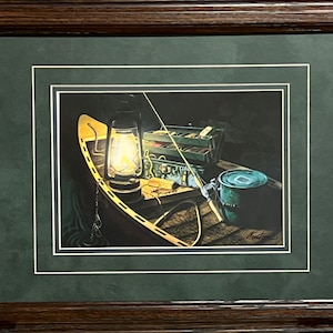 May include: A framed print of a painting depicting a wooden boat with fishing gear, a lantern, and a tackle box. The lantern is lit and casting a warm glow on the scene. The painting is set against a dark background.