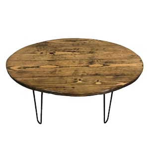 May include: A round wooden coffee table with a natural wood finish and black hairpin legs.