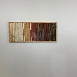 May include: A rectangular wall art piece made of wood slats in various shades of brown, beige, and white. The slats are arranged in vertical rows, creating a gradient effect.