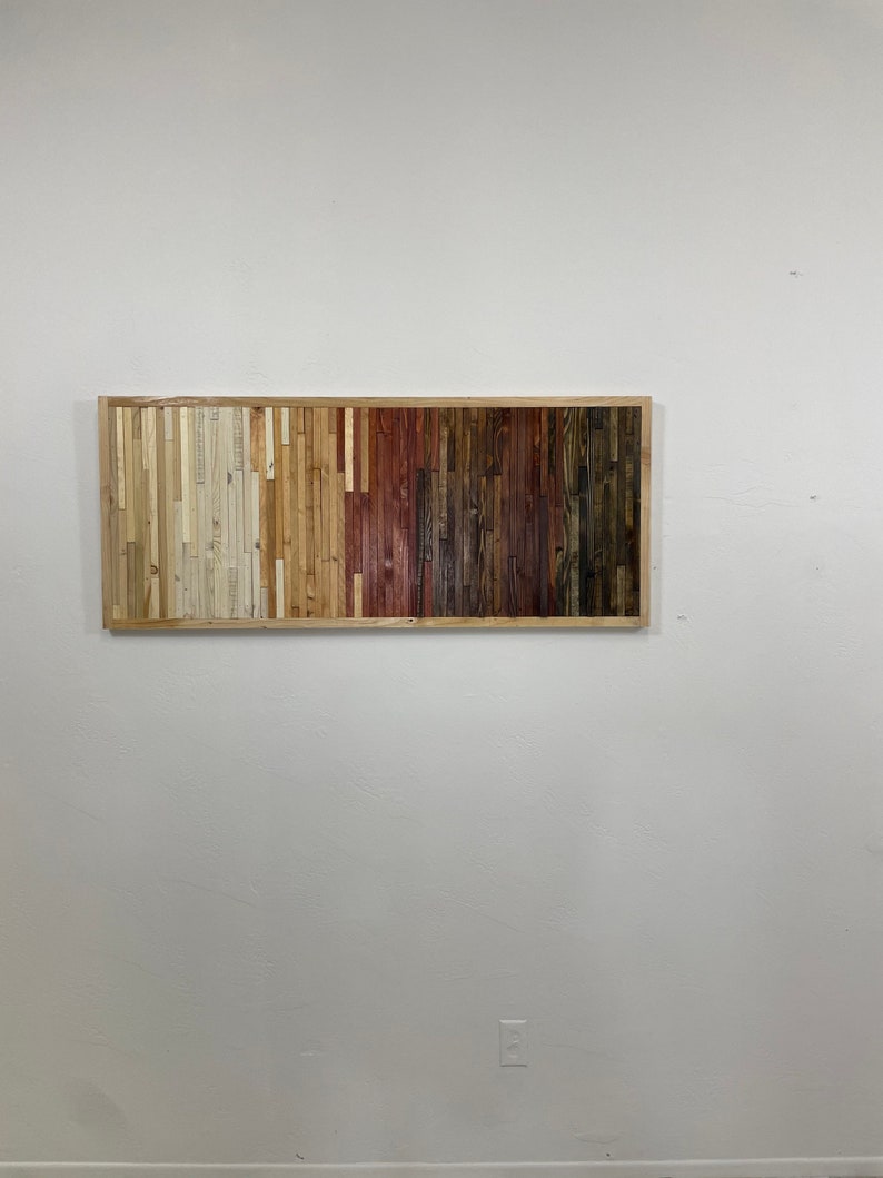 May include: A rectangular wall art piece made of wood slats in various shades of brown, beige, and white. The slats are arranged in vertical rows, creating a gradient effect.