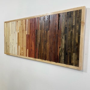 May include: A rectangular wooden wall art piece with a natural wood frame. The wood is arranged in a horizontal pattern with varying shades of brown, red, and white.