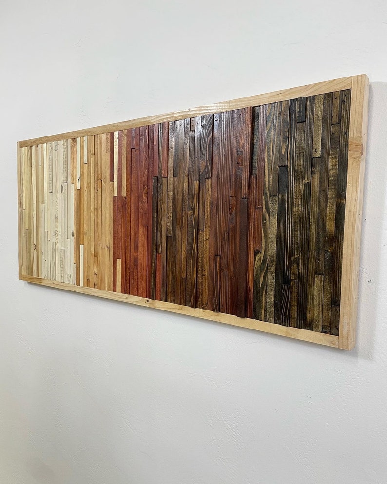 May include: A rectangular wooden wall art piece with a natural wood frame. The wood is arranged in a horizontal pattern with varying shades of brown, red, and white.