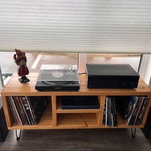May include: A wooden record player stand with three shelves. The top shelf has a black record player with a clear lid, a black amplifier, and a red Iron Man hand figurine. The bottom shelves are filled with vinyl records.